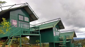 A green building with multiple levels and staircases, surrounded by vegetation. - Coorg Tree House Tent (Madikeri)