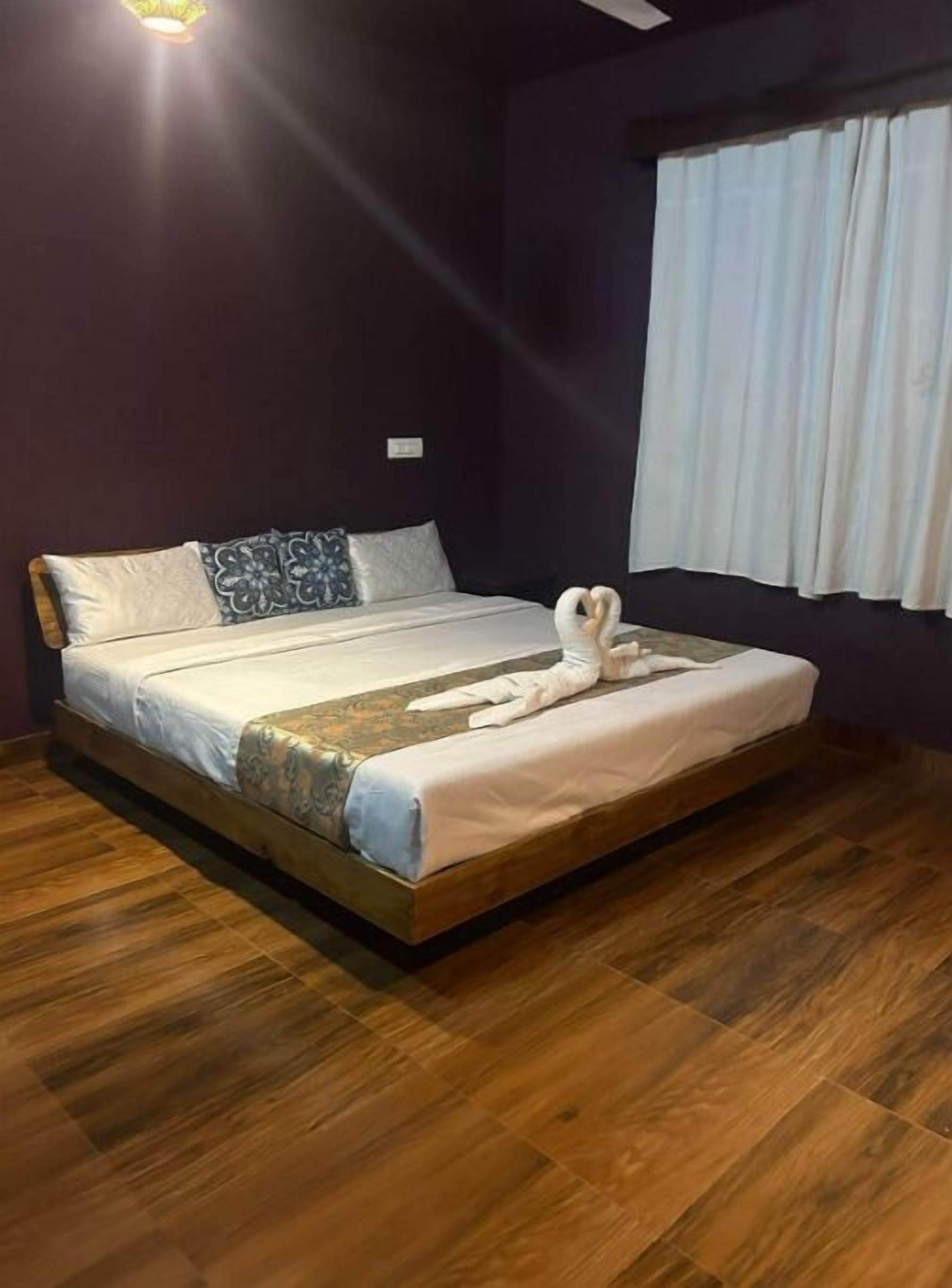 A neatly made bed with a heart-shaped towel, a patterned throw, and a decorative pillow.