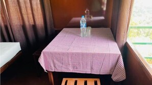 Um quarto pequeno com toalha de mesa xadrez, um banco de madeira e uma janela com cortinas.