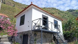 Een wit gebouw met een balkon en een stenen fundament, omgeven door groen en heuvels.