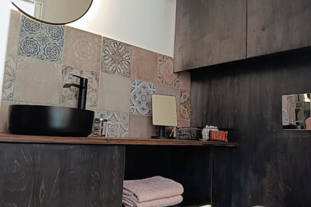Een badkamer met een zwart wastafel, een spiegel en decoratieve tegels aan de wand.