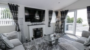 A modern living room with a fireplace, a flat-screen TV, and a balcony with a view. - Manor Heights Lodge (Wemyss Bay)
