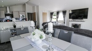 A modern living room with a dining area, a kitchen, and a TV mounted on the wall. - Manor Heights Lodge (Wemyss Bay)