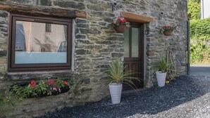 A stone building with a wooden door, windows, and hanging flower baskets. - Old Post Office Cottage (Ulverston)