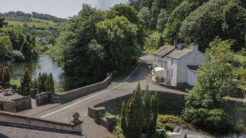 A riverside road with a white building, a stone wall, and greenery.