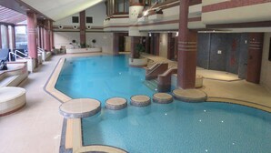 An indoor swimming pool with multiple levels, seating areas, and a tiled floor. - Old Post Office Cottage (Ulverston)