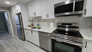 A modern kitchen with stainless steel appliances, white cabinetry, and a marble backsplash.