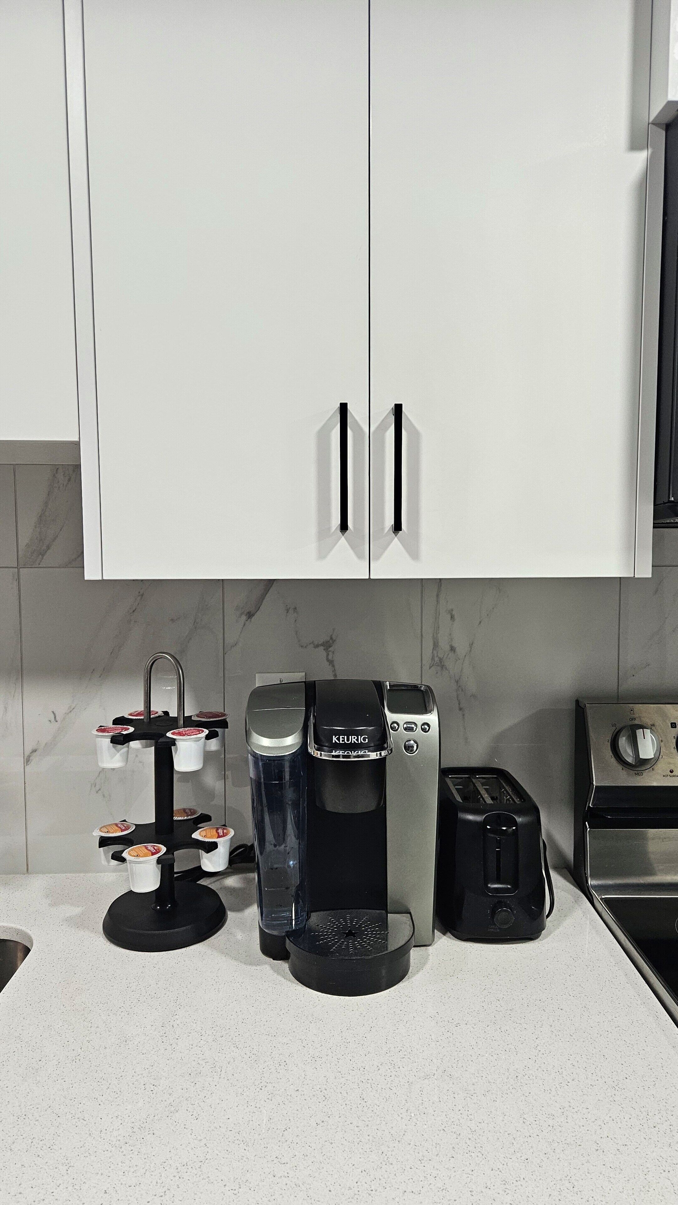 Uma cozinha moderna com armários brancos, cafeteira, torradeira e chaleira no balcão.