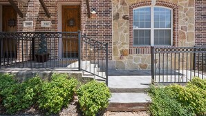 A brick building with numbered doors, a stone arch window, and a metal railing.