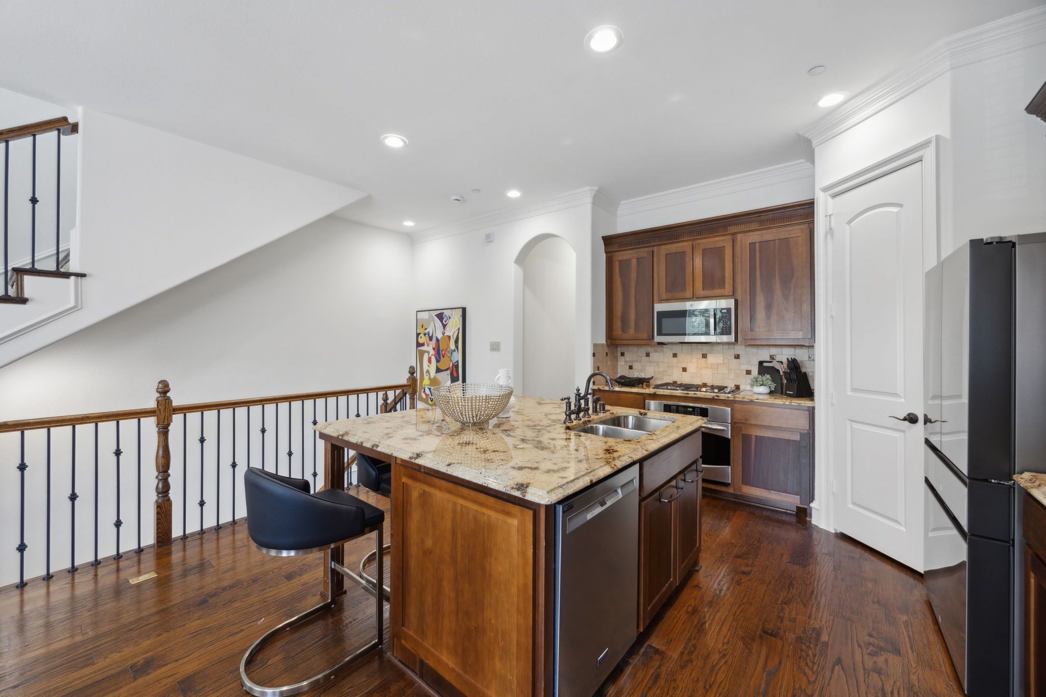 A kitchen with a central island, wooden cabinets, stainless steel appliances, and a staircase with a railing.