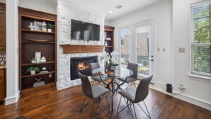 A dining area with a stone fireplace, a TV mounted above it, and a view of the outside through large windows.