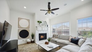 A spacious living room with a fireplace, a ceiling fan, and a large window offering a view of the outside.