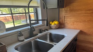 Une cuisine équipée de deux éviers en acier inoxydable, d’une fenêtre donnant sur un jardin, et d’un panier de citrons posé sur le plan de travail.