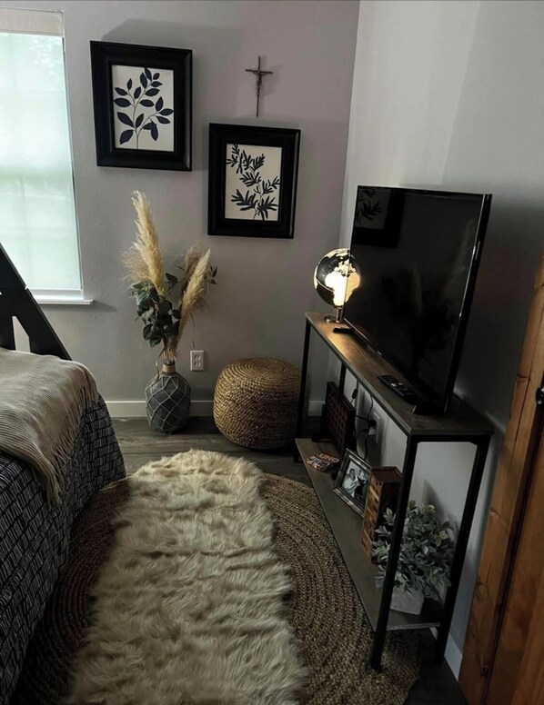 A cozy living room with a sofa, a round rug, a TV on a stand, and wall art. - Dominic House, a charming VRBO in Krebs, Oklahoma (McAlester)