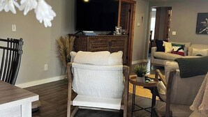 Un salon comprenant un fauteuil en bois, un canapé, un téléviseur et un coin repas avec une table.