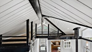 Ein Zimmer mit hohen Decken, freiliegenden Balken, einer Treppe und einem sichtbaren Kamin.