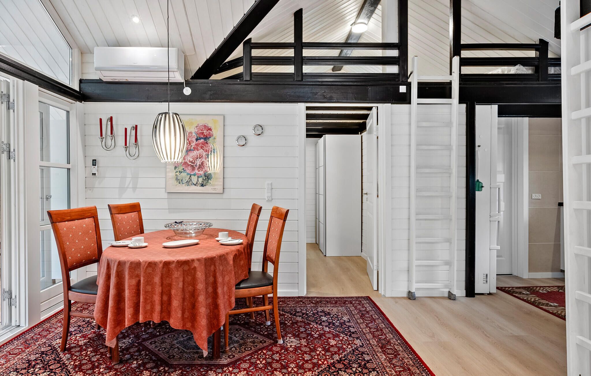 A dining area with a round table, six chairs, and a red patterned rug.