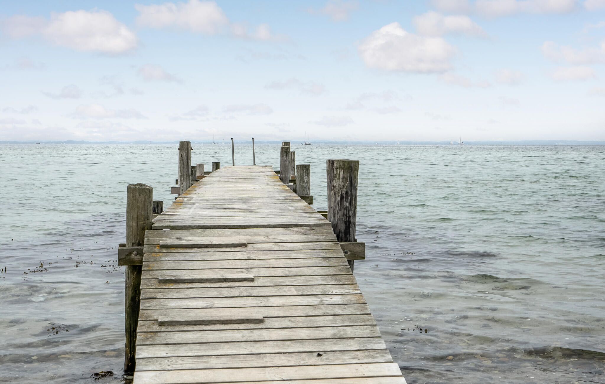 Une jetée en bois s’étendant sur une étendue d’eau calme, sous un ciel dégagé.
