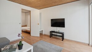A modern living room with a wooden ceiling, a flat-screen TV mounted on the wall, a small table with a remote control, and a grey rug on the floor. - Awesome home in Sydals with WiFi (Sydals)