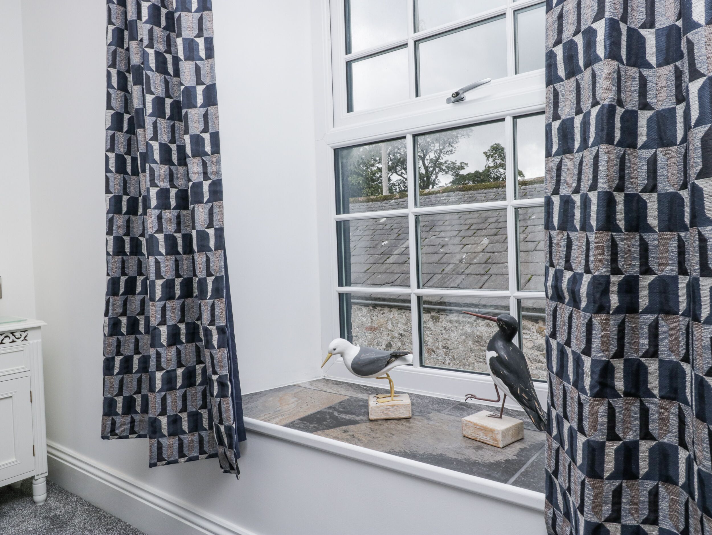 A bathroom with a window, a white cabinet, and a bird figurine on a windowsill.