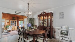 Ein Esszimmer mit Holztisch, Stühlen, einer Chandelierleuchte, einem Glasvitrinen-Schrank und einem hochaufliegenden Kinderstuhl.