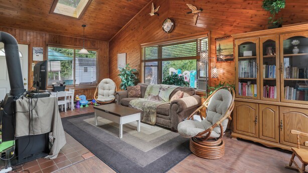 Ein gemütliches Blockhäuschen im Inneren mit Holzbalkendecke, Kamin, Sofa, zwei Sesseln, Bücherregal und Essbereich.