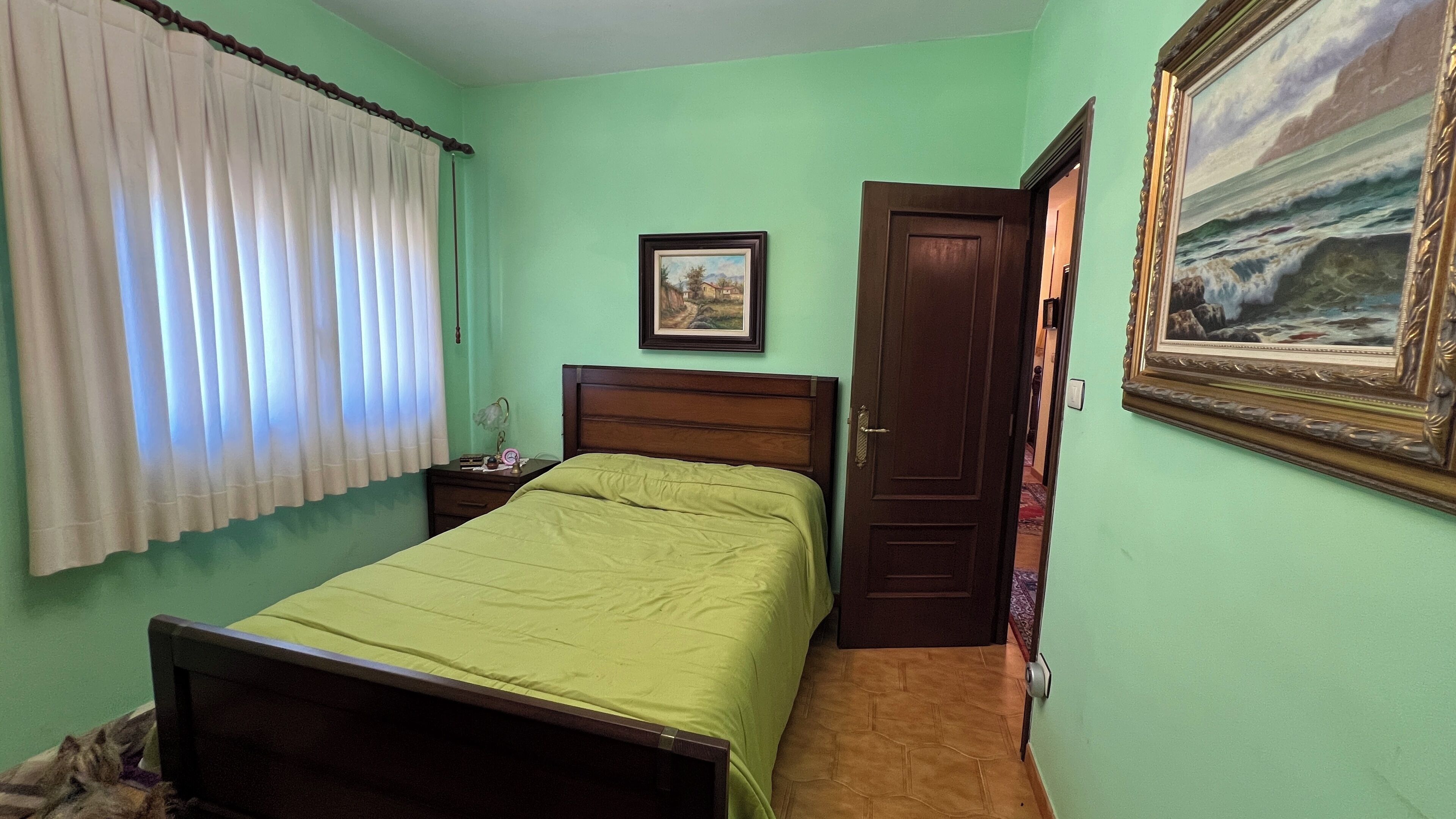 Une chambre à coucher avec un lit, une table de chevet, une porte et un tableau au mur.