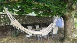 A hammock set up between trees, a table with chairs, and a blue gate in the background. - House located in the Fragas do Eume Natural Park, ideal for families. (Monfero)