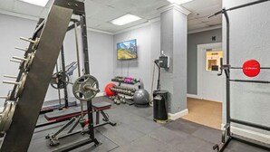 Ein Fitnessraum mit Krafttrainingsgeräten, einem an der Wand montierten Fernseher und einer Tür mit einem roten Schild.