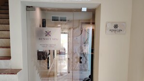 Entrada de un spa con puerta de vidrio, un letrero que dice "SPA Sunset Resorts" y una planta en maceta a la derecha.