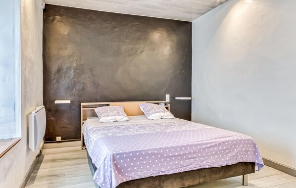 A bedroom with a bed, pillows, a bedside table, and a wall-mounted heater.