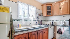 A kitchen with wooden cabinets, a sink, a stove, and a window with curtains. - Beautiful home in Le Muy with WiFi (Le Muy)