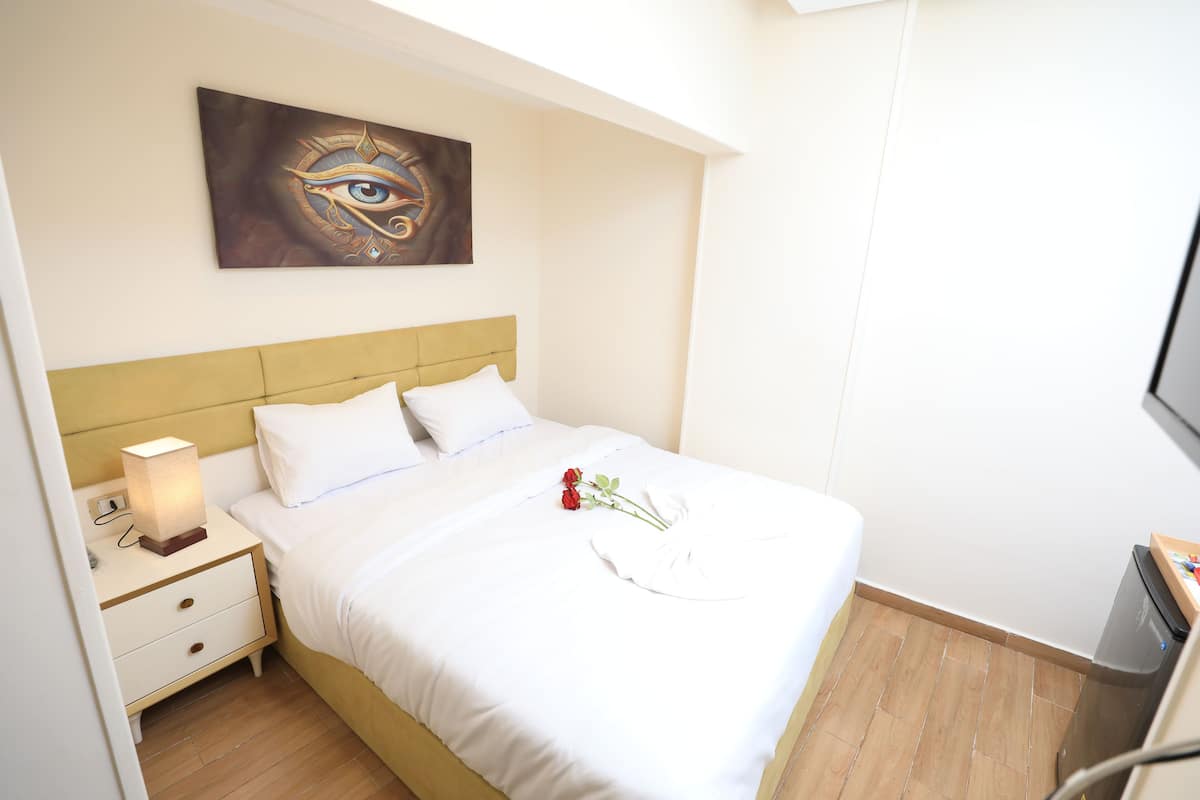 A neatly made bed with white linens, a bedside lamp, and a single red rose on the bed.