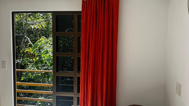 Une pièce dotée d’une porte-fenêtre coulissante donnant sur un balcon, d’un fauteuil marron et d’un appareil de climatisation fixé au mur.