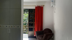 Une pièce avec un sol carrelé, un fauteuil marron, une fenêtre avec des rideaux rouges et un climatiseur fixé au mur.