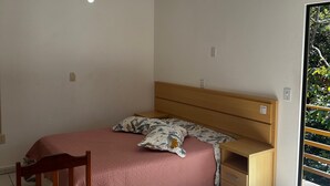 Une chambre à coucher comprenant un lit, une table de chevet en bois, une chaise, un ventilateur de plafond et une fenêtre donnant sur un paysage verdoyant.