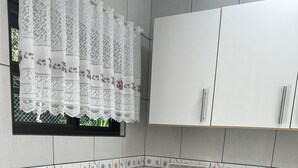 Une cuisine avec des meubles blancs, un plan de travail en granit, une cuisinière noire, un évier et une fenêtre ornée de rideaux en dentelle.