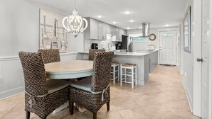 A modern kitchen with white cabinets, a central island, and a dining area with wicker chairs.