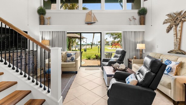 A spacious living area with a staircase, two sofas, a coffee table, and a view of a playground through large glass doors.