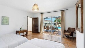 Une chambre d’hôtel avec deux lits, une petite table sur laquelle est posé un vase, une chaise, une grande fenêtre avec des rideaux et une vue sur une piscine et les bâtiments environnants.