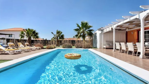 Une piscine entourée de palmiers, avec des chaises longues et des parasols, ainsi qu’un espace de repos abrité.