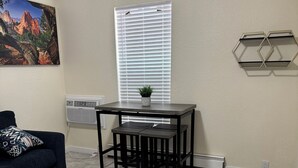 Un salon avec un canapé bleu foncé, une petite table sur laquelle est posée une plante en pot et une fenêtre avec des stores.