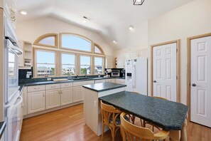 Una cocina con una isla central, armarios de madera, horno empotrado y vistas a casas a través de amplias ventanas.