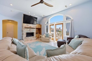 A living room with a stone fireplace, a flat-screen TV, a ceiling fan, and a large window with a view.