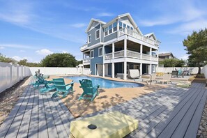 Una casa de dos pisos con piscina, sillas de deck y una valla blanca.