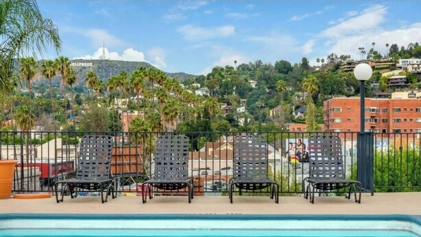 A poolside area with lounge chairs and a view of a hill with the Hollywood sign in the background.