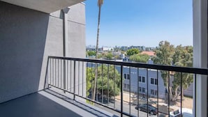 A balcony with a metal railing overlooking a cityscape, including buildings and a palm tree.