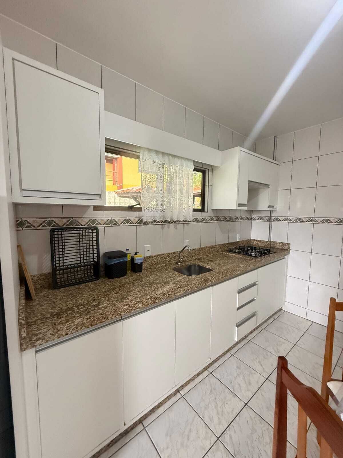 A kitchen with white cabinets, a granite countertop, a sink, and a window with a lace curtain.