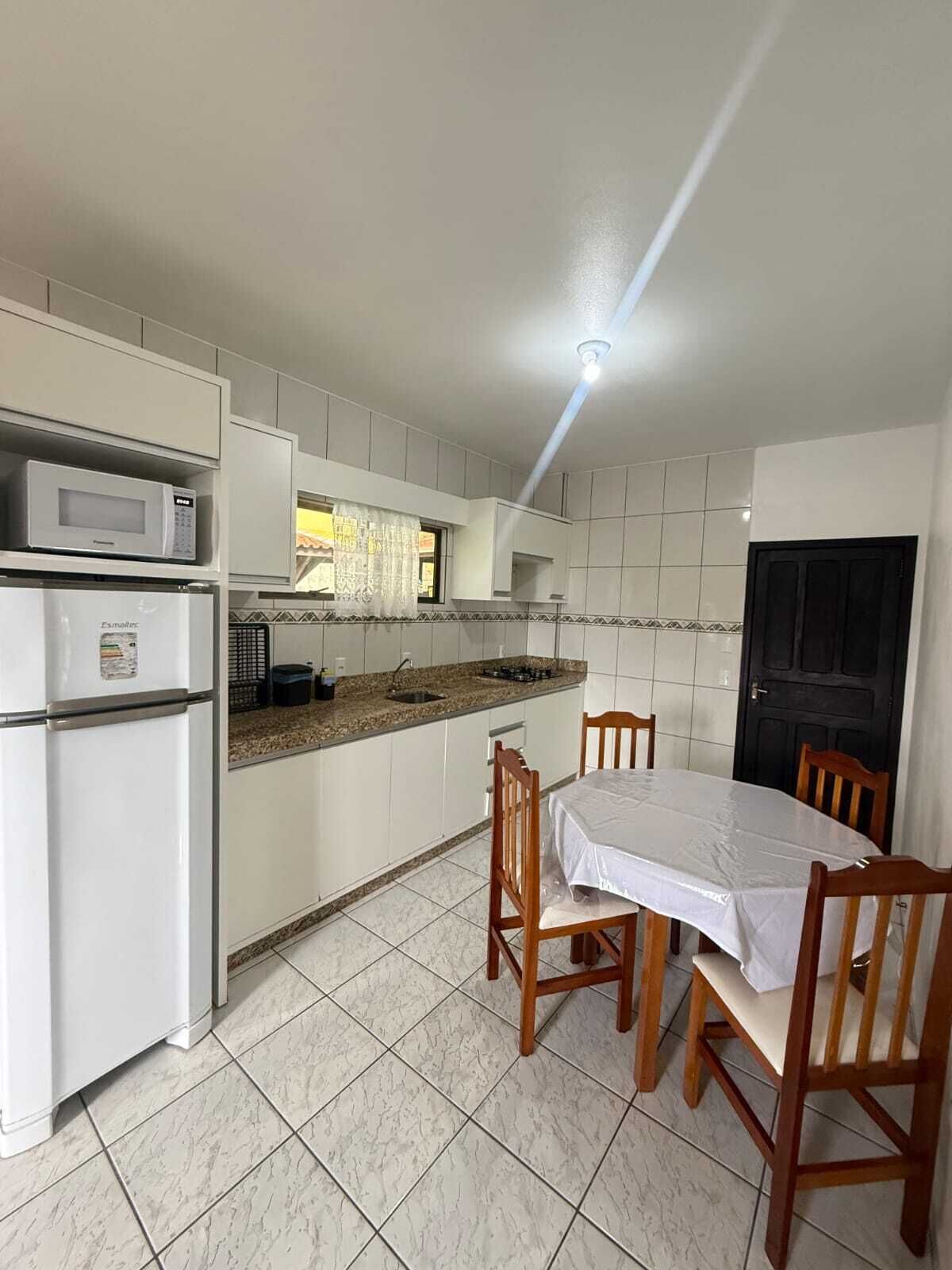 A compact kitchen with white cabinets, a microwave, a sink, and a dining table with chairs.