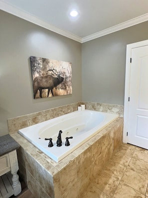Een badkamer met een groot bad, een kunstwerk van een eland aan de muur, en een deur aan de rechterkant.
